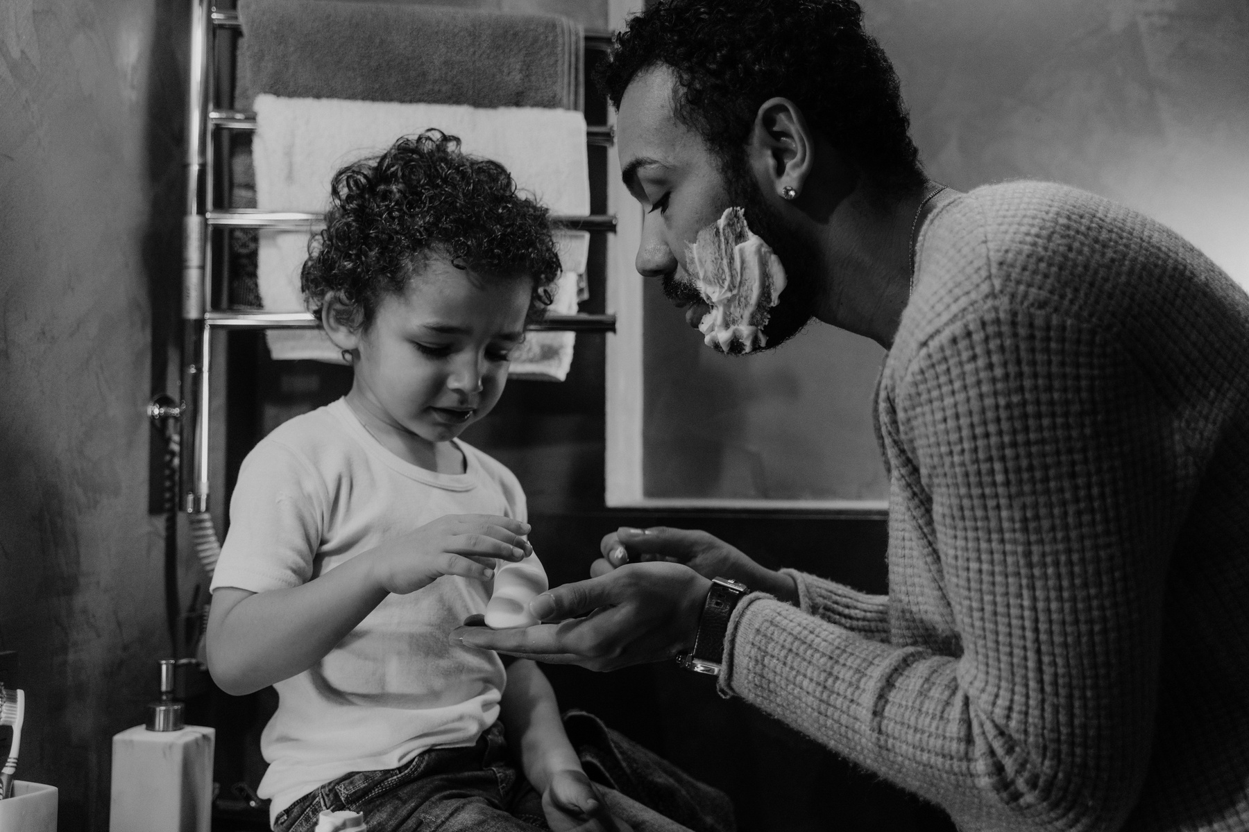 A Grayscale Photo of a Man with Shaving Cream on His Face while Talking to His Son